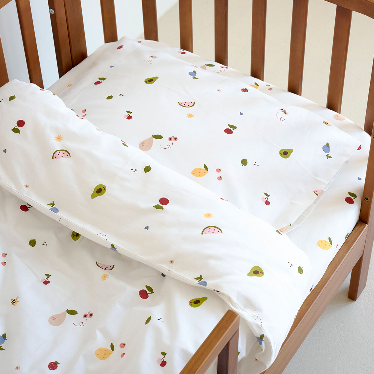 Parure de lit enfant en coton blanc 120x150 avec motifs fruits colorés, installée dans un lit en bois naturel