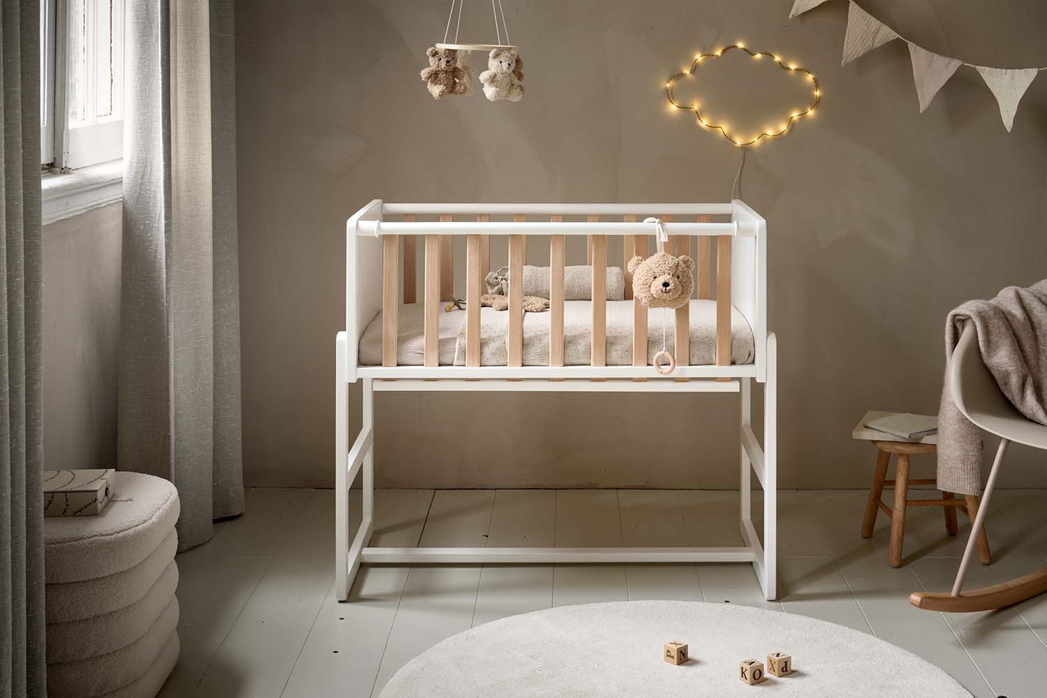 Berceau cododo blanc et bois installé dans une chambre bébé douce et naturelle, avec mobile en peluche et décoration lumineuse en forme de nuage.