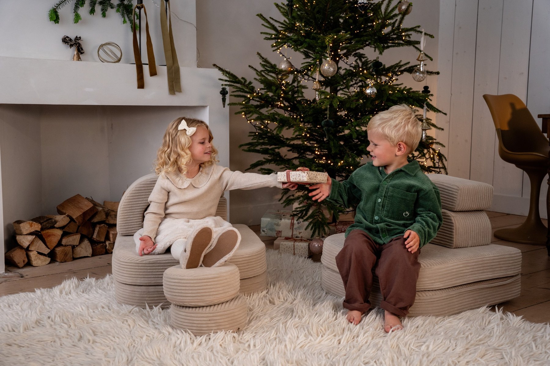 Deux enfants s'offrent un cadeau près du sapin de Noël