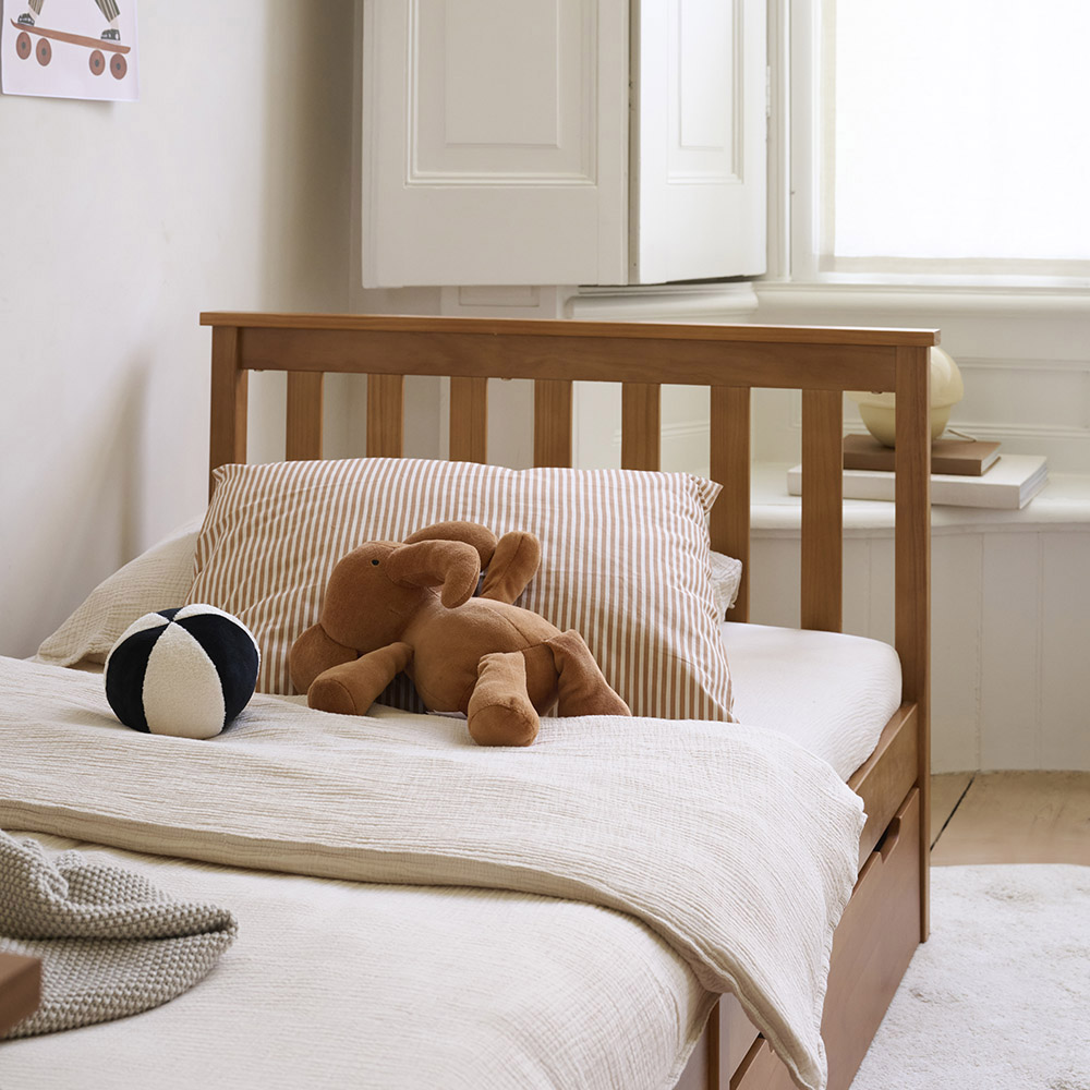 Lit enfant Milo 90x200 en bois couleur noyer, habillé d’une parure de lit en gaze de coton beige avec coussin rayé et peluches, dans une chambre enfant au style naturel.