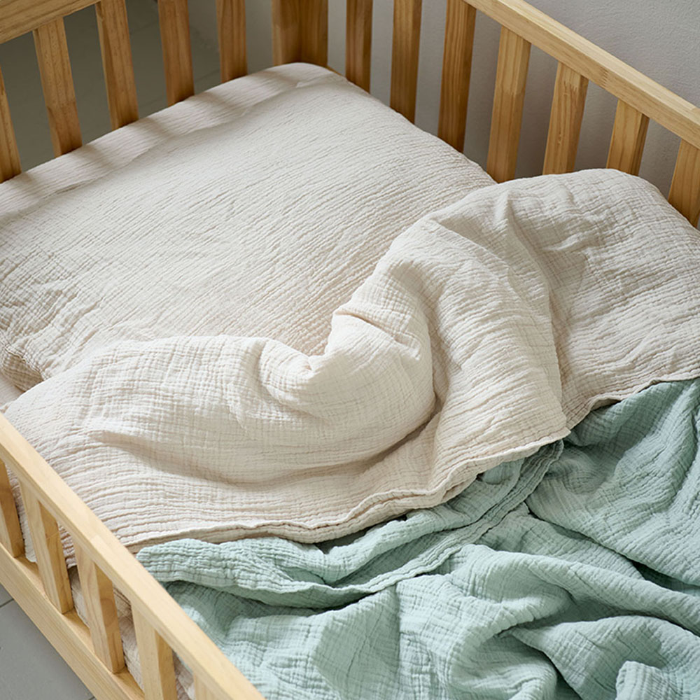 Parure de lit enfant en gaze de coton beige Petite Amélie, installée dans un lit en bois naturel, offrant une texture douce et respirante